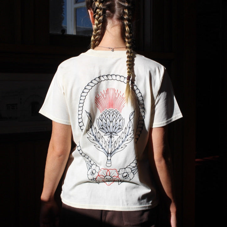 Person wearing a white t-shirt with a graphic design on the back, standing in a dark room.